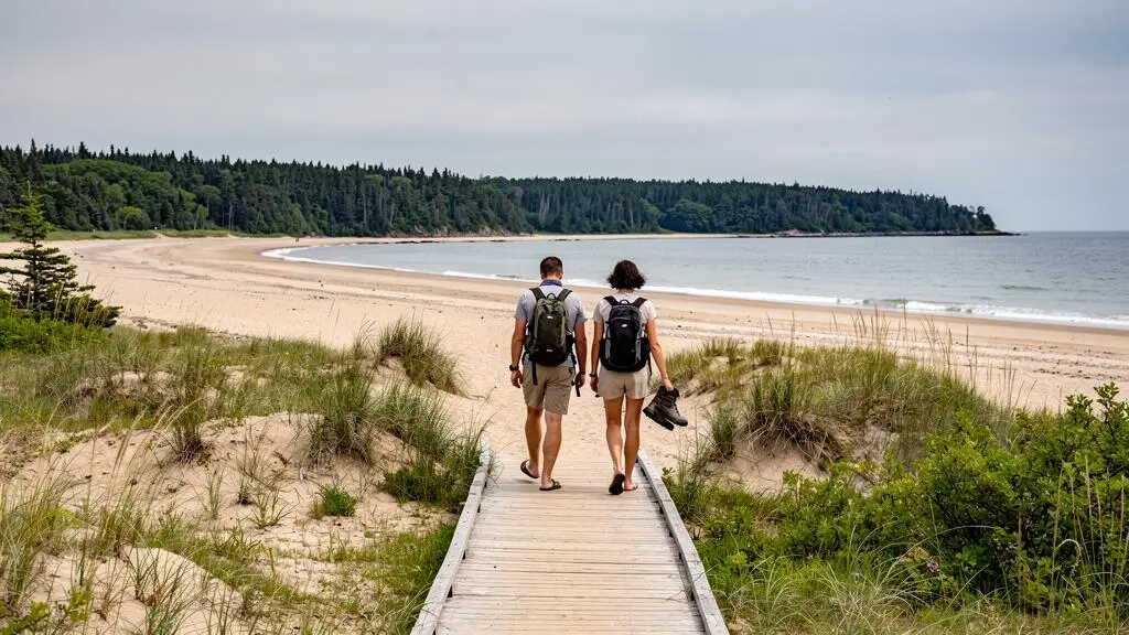 Deux voyageurs empruntent une passerelle en bois menant à une plage peu fréquentée bordée de dunes au Nouveau-Brunswick.